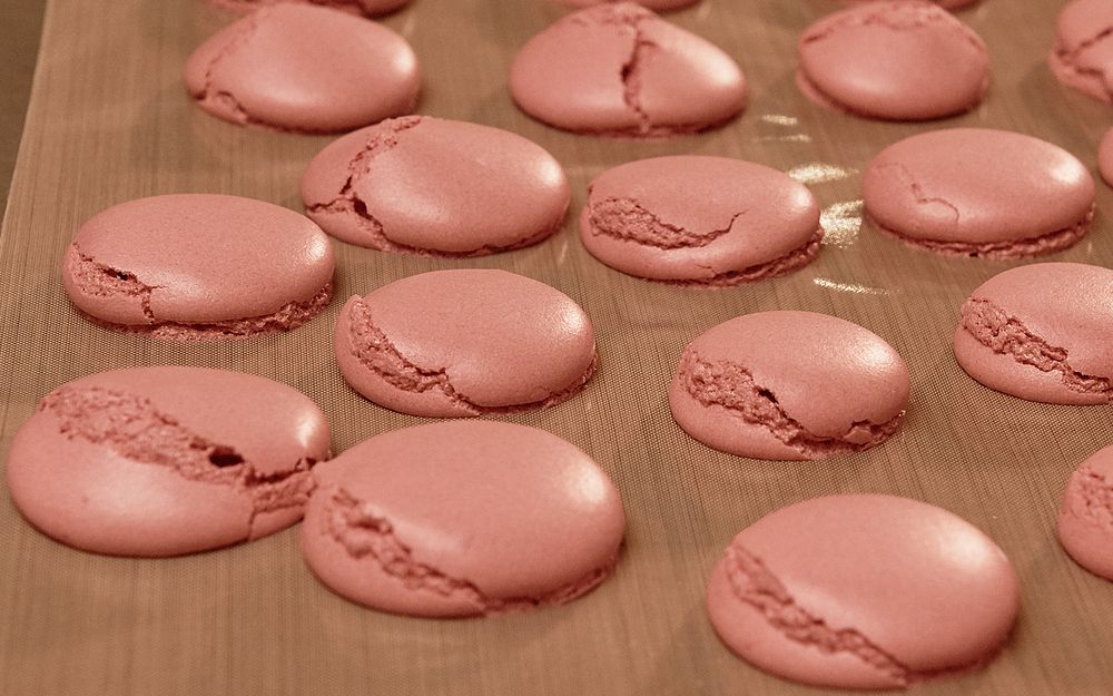 A tray of cracked macarons on a silicone mat.