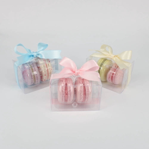 A selection of wedding favours. Two macarons in clear plastic boxes tied with ribbon.